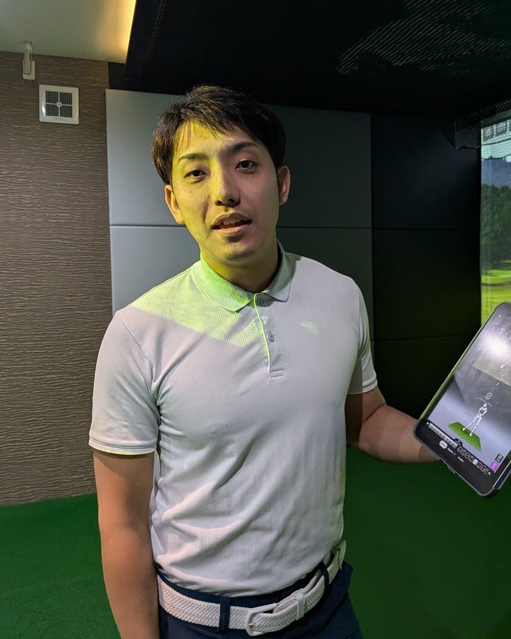 Ikko Yamazaki holding a phone showing a 3D swing analysis in a golf studio